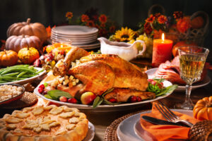 Roast turkey, pumpkin pie, beans, potatoes, gravy, folded orange napkin with fork and knife, lit candle, whole squashes
